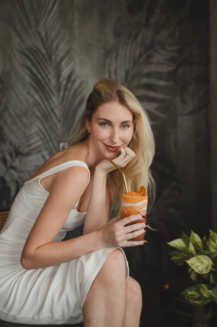 A guest with a fresh citrus smoothie against the palm-painted wall